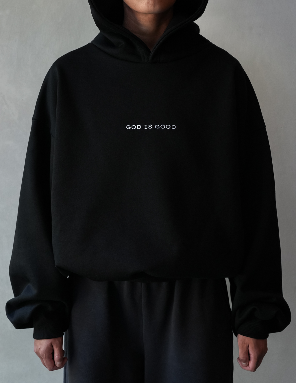 Person wearing a black hoodie with 'GOD IS GOOD' text on a gray background