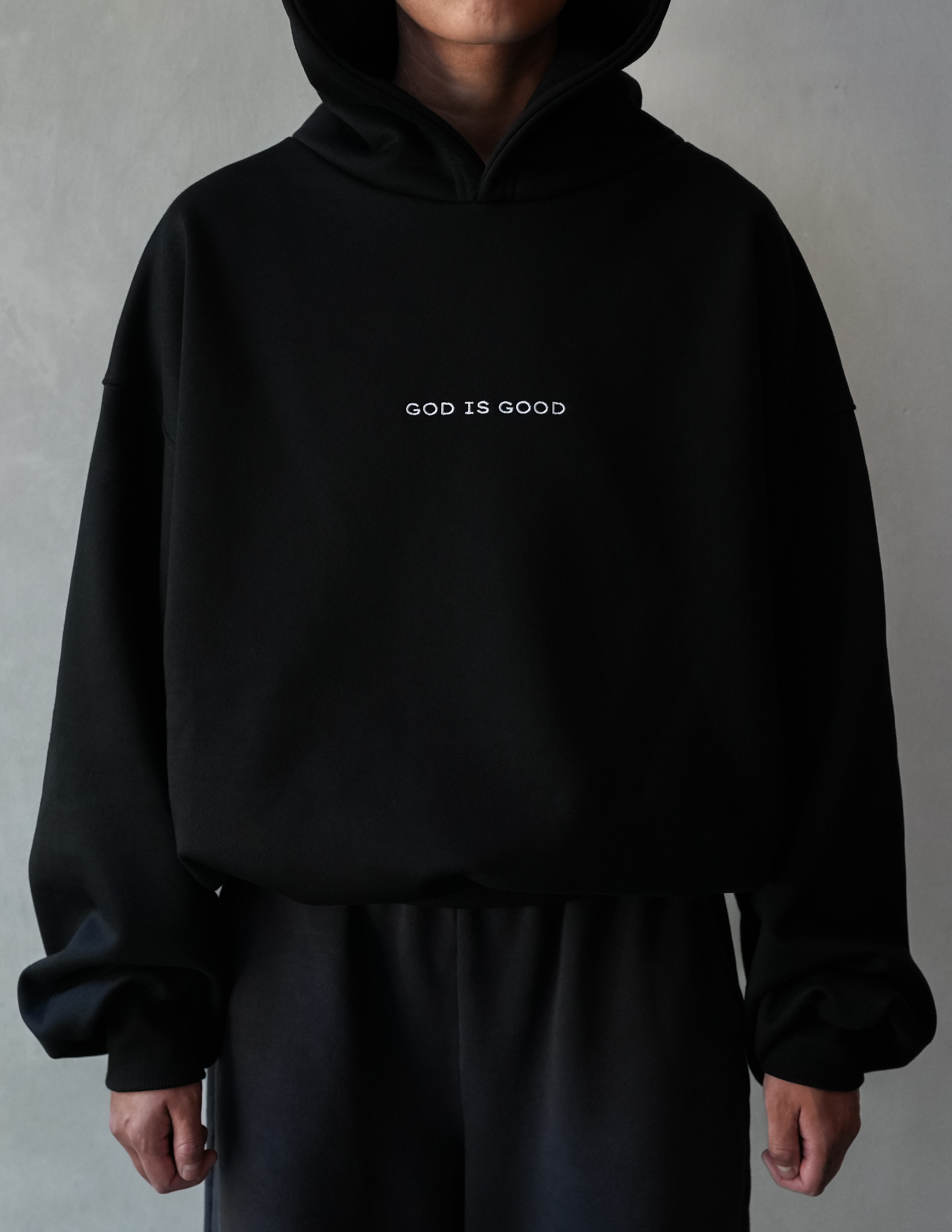 Person wearing a black hoodie with 'GOD IS GOOD' text on a gray background